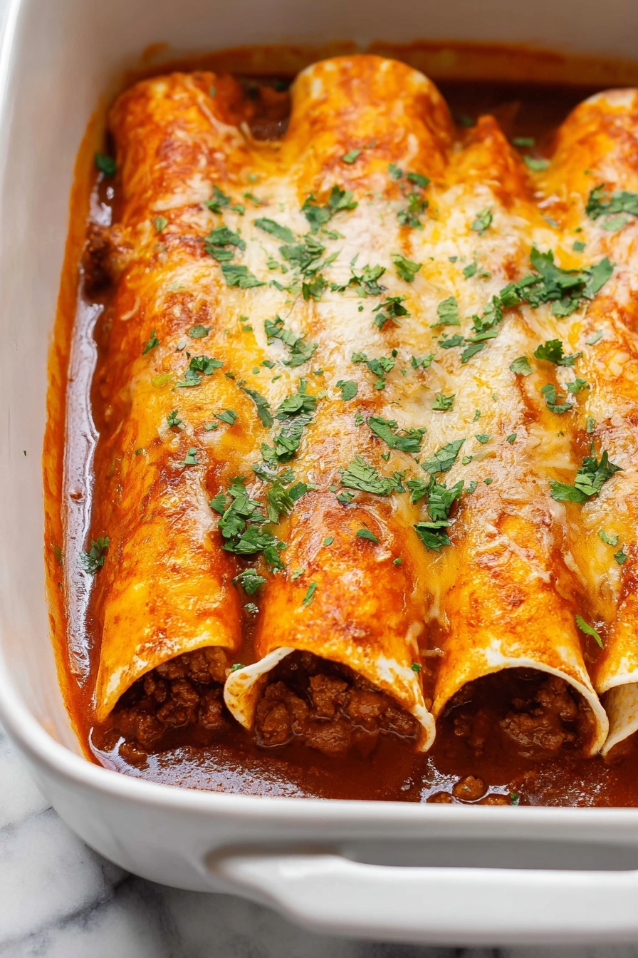 Beef Enchiladas - The image shows a white baking dish filled with four rolled enchiladas placed side by side. Each enchilada is covered with a thick, bright orange-red sauce and melted cheese that is slightly golden and smooth in texture. Inside the enchiladas, you can see a rich, dark brown meat filling that looks moist and chunky. Fresh, chopped green cilantro is sprinkled evenly on top, adding a pop of color. The sauce inside the dish pools slightly around the bottom edges, giving a saucy and inviting look. The dish is sitting on a white marbled surface. Photo taken with an iphone --ar 2:3 --v 7