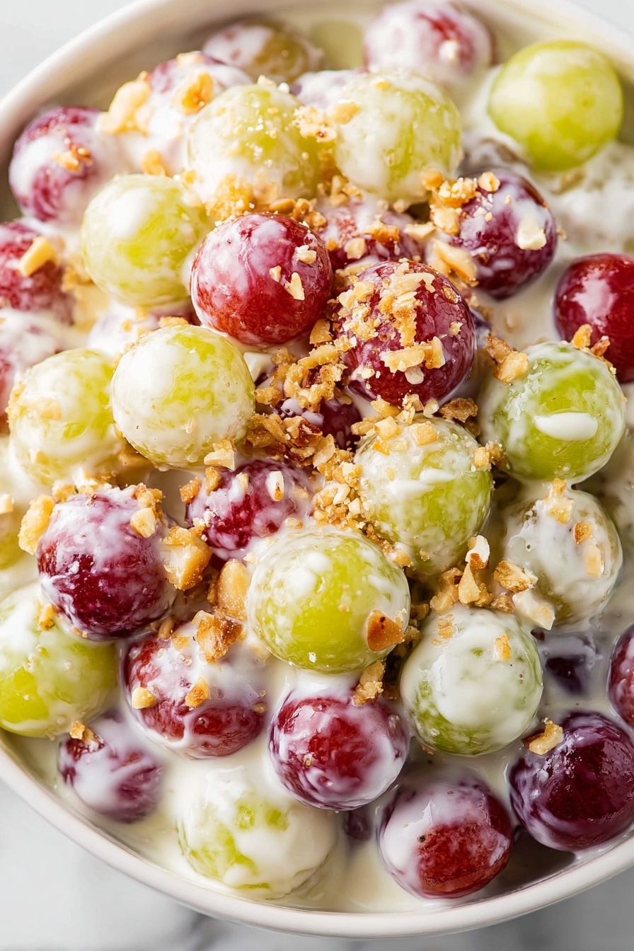 The image shows a close-up of a white bowl full of small round grapes in red, green, and yellow colors, all covered in a thick, creamy white sauce. On top of the grapes and sauce are small pieces of chopped nuts, adding a light brown texture and contrast. The grapes are tightly packed and glossy from the sauce, creating a rich and creamy look. The background features a white marbled texture. photo taken with an iphone --ar 2:3 --v 7