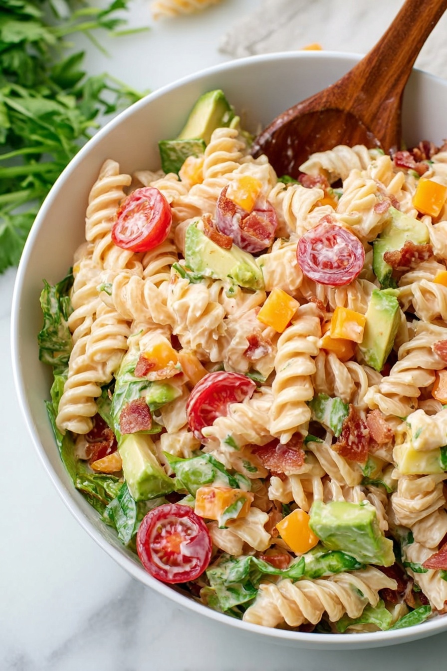 A white bowl filled with a creamy spiral pasta salad showing about four layers: the base layer has light beige spiral pasta with a smooth texture; scattered throughout are bright red halved cherry tomatoes with a shiny surface; small cubes of orange cheddar cheese add pops of color; chunks of green avocado with a soft texture are mixed in; pieces of green leafy lettuce add freshness around the edges; bits of crispy bacon are visible in reddish-brown strips; everything is coated lightly in a creamy dressing giving a slight gloss; a wooden spoon rests on the side inside the bowl; the bowl sits on a white marbled surface with some green herbs blurred in the background photo taken with an iphone --ar 2:3 --v 7