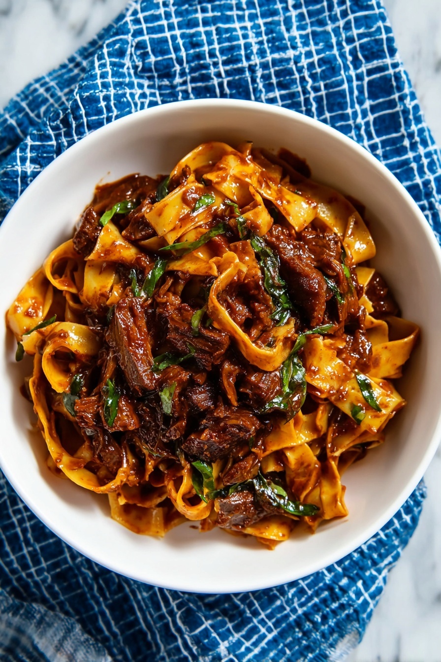 The image shows a white bowl filled with a rich, dark brown noodle dish. The noodles are thick and coated with a glossy sauce mixed with small pieces of green herbs and chopped green onions scattered on top. There are bits of crushed peanuts sprinkled over the noodles, adding texture. The bowl sits on a blue cloth with a white dotted line pattern, placed on a white marbled surface. In the background, there is a blurred red kitchen appliance. The photo taken with an iphone --ar 2:3 --v 7