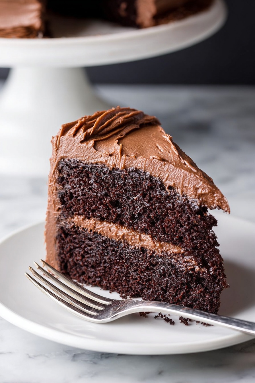 A slice of chocolate cake with two thick, dark brown layers that look soft and moist, separated and covered by a smooth, rich chocolate frosting that is light brown and creamy. The frosting also covers the outer sides of the cake, spreading unevenly with soft peaks and swirls. The cake sits on a white plate with a silver fork lying beside it, all placed on a white marbled surface. In the background, the base of a white cake stand is partially visible. photo taken with an iphone --ar 2:3 --v 7