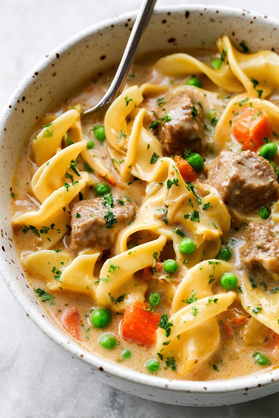 This image shows a creamy soup full of layers with wide egg noodles that are light yellow and curled, floating on the top layer. There are chunks of browned beef with a textured surface scattered throughout the soup, adding depth. The soup also has bright orange carrot pieces and vibrant green peas mixed in, giving a nice color contrast. The creamy broth has a light beige color with hints of spices and small green herb pieces sprinkled evenly on top and around the dish. A ladle with a golden handle is lifting some noodles, beef, and vegetables in the center of the bowl. The dish is in a white bowl placed on a white marbled surface. Photo taken with an iphone --ar 2:3 --v 7