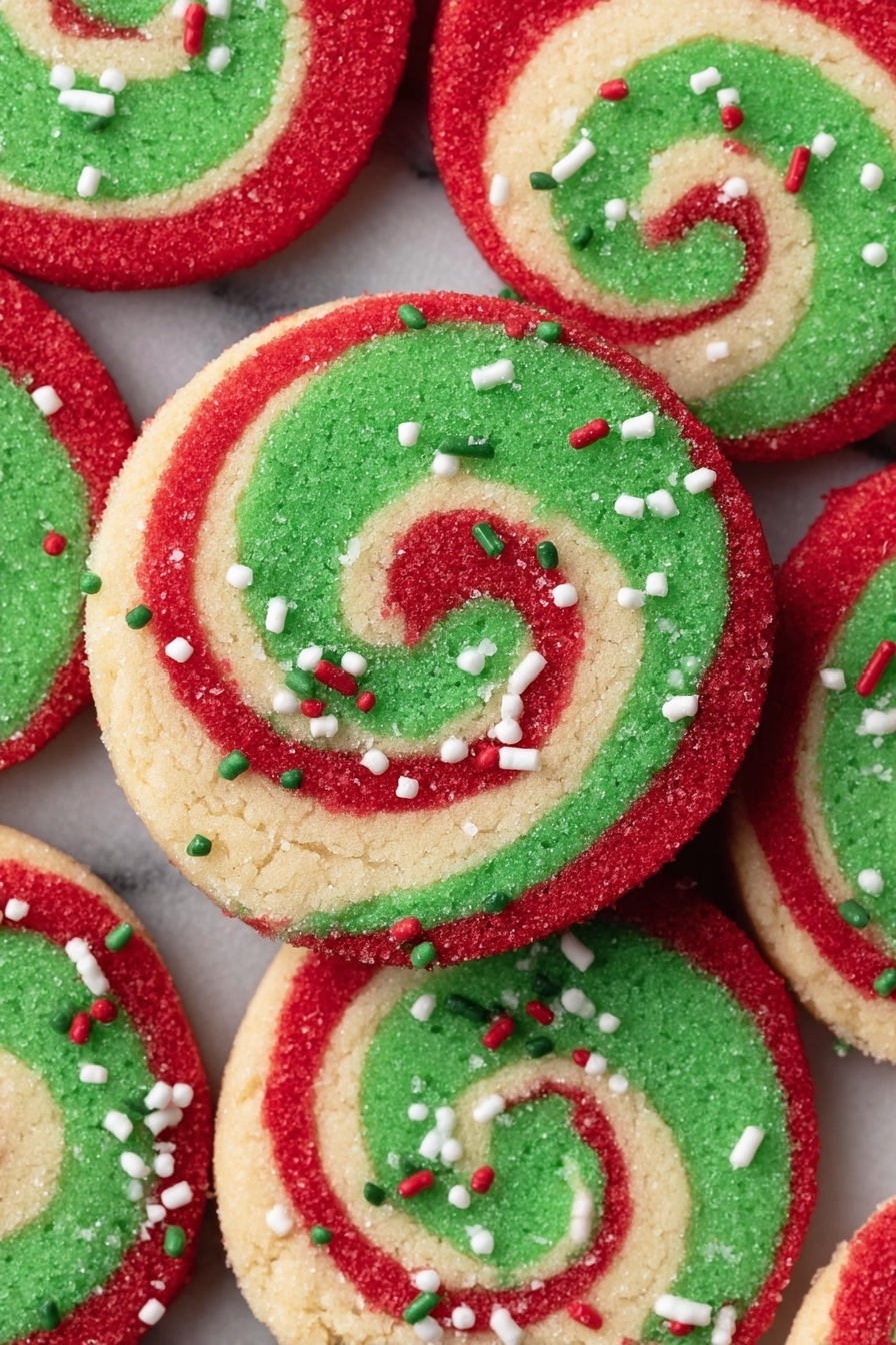 The image shows a close-up of round swirl cookies arranged closely together on a white marbled surface. Each cookie has three visible layers: a bright green inner spiral, a thin beige middle spiral, and a thicker red outer spiral. The edges of the cookies are covered with red sugar and decorated with small white, green, and red sprinkles, giving a festive look. The texture of the cookies looks soft and slightly grainy from the sugar coating. Photo taken with an iphone --ar 2:3 --v 7