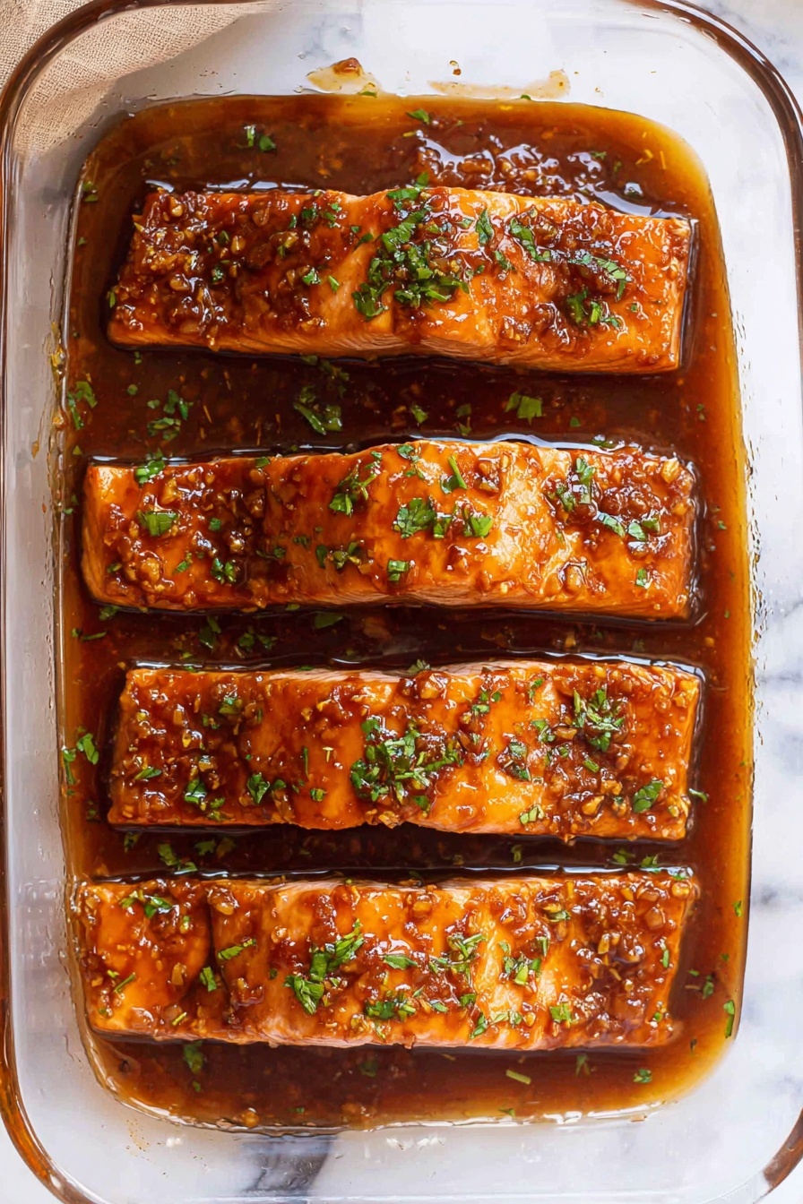 The image shows four rectangular pieces of cooked salmon placed side by side in a clear glass baking dish, lined with light brown parchment paper. Each salmon piece is coated with a thick, shiny dark orange-brown sauce that looks sticky and has small bits of garlic or spices on the surface. Garnishes of finely chopped fresh green herbs are sprinkled on top of each piece, adding contrast to the warm tones of the salmon and sauce. The baking dish is resting on a surface with a white marbled texture, and the sauce has slightly pooled around the salmon inside the parchment paper, showing a glossy finish. photo taken with an iphone --ar 2:3 --v 7