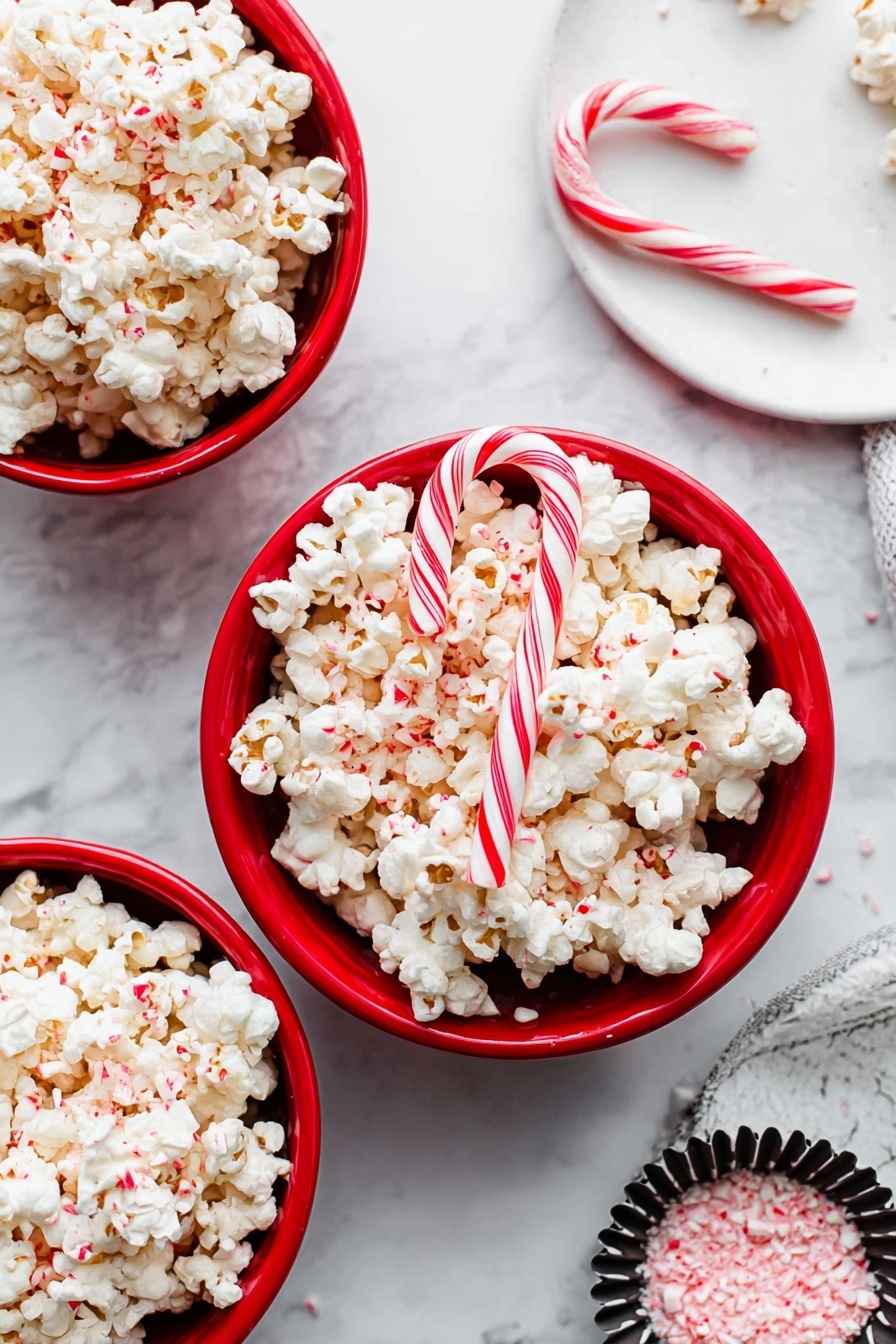 Three red bowls filled with white popcorn that has small red peppermint bits sprinkled on top. Two candy canes with red and white stripes rest diagonally on the popcorn in the center bowl. One more candy cane lies flat on the white marbled surface near the bowls. In the upper right corner, part of a white plate with a black and white striped cupcake liner and some pink crushed candy is visible. The scene is brightly lit with a clean, festive look. photo taken with an iphone --ar 2:3 --v 7