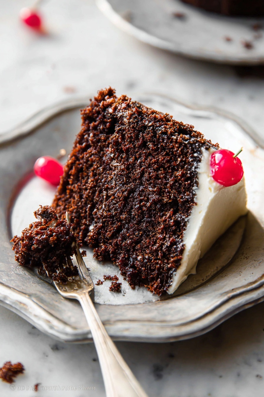 A single slice of dark brown chocolate cake sits on a shiny white plate with a slightly wavy edge. The cake has one thick layer showing a moist, crumbly texture and a thin layer of light cream frosting visible along the bottom edge. A small red cherry rests on top near the edge. In front of the slice, a silver fork holds a small bite of cake with some cream frosting. A few crumbs and a second red cherry are scattered around the plate on a white marbled surface. Photo taken with an iphone --ar 2:3 --v 7