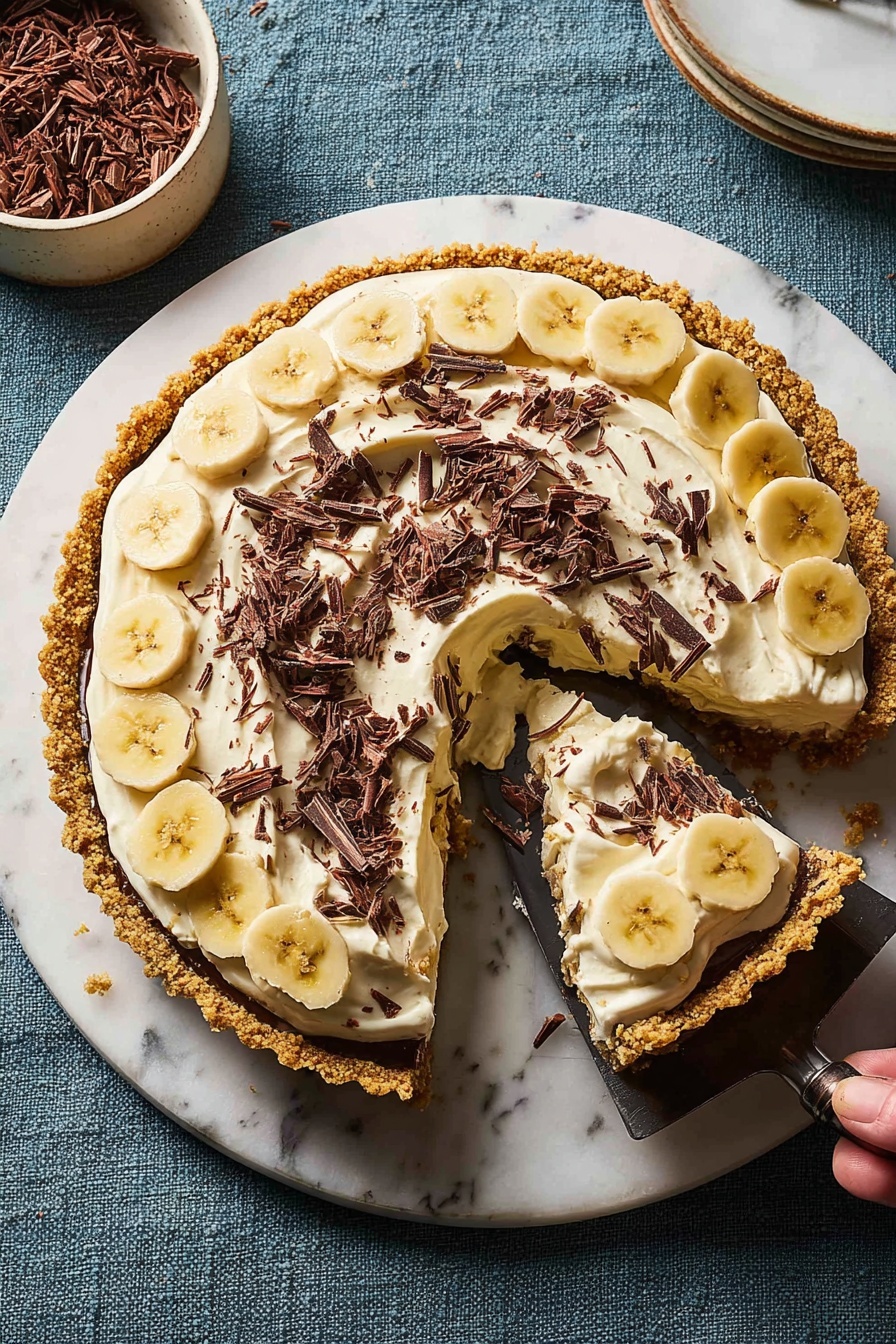 A round pie sits on a white marbled board with a golden crumbly crust forming the base and edges. Inside the crust, thin, round slices of pale yellow bananas form a neat layer just beneath a large thick layer of creamy white topping spread unevenly with swirled textures. On top of the cream, small dark brown chocolate shavings are scattered all over, adding contrast. One slice is being lifted out with a dark knife attached to a woman's hand, revealing the smooth thickness of the filling inside. The background is a textured blue cloth with a white bowl holding more chocolate shavings at the top left corner. photo taken with an iphone --ar 2:3 --v 7