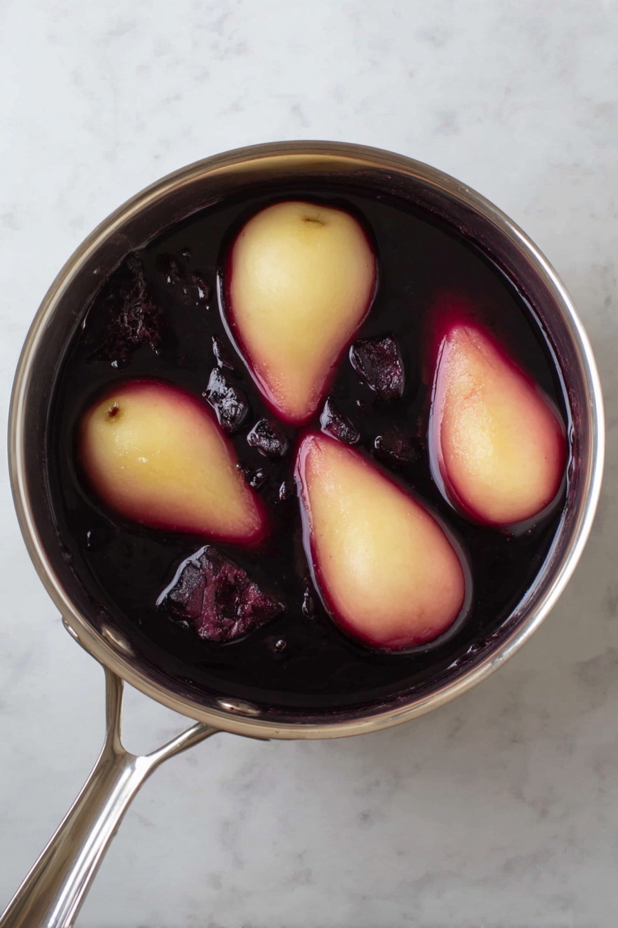 The image shows two poached pears with a shiny deep red color placed on top of bright orange slices on a white plate with a delicate blue floral design. Around the pears, there are scattered green pistachio pieces and three cinnamon sticks lying next to the orange slices. The pear stems are dark brown, adding contrast to the smooth red pears, while a small amount of red syrup pools beneath the orange slices. The plate is set on a white marbled surface with a rustic wooden table partially visible in the background. Photo taken with an iphone --ar 2:3 --v 7