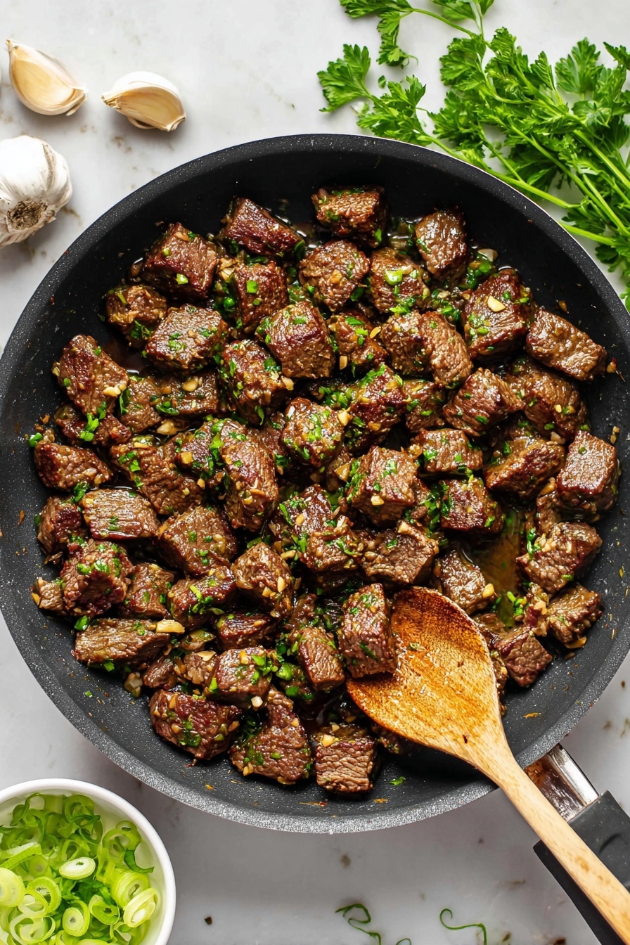 The image shows a black frying pan filled with many small, browned cubes of cooked beef mixed with finely chopped green herbs and small bits of garlic. The beef pieces have a shiny, slightly textured surface from cooking. A wooden spoon rests inside the pan, touching some of the beef cubes on the right side. Around the pan, on a white marbled surface, there are some sprigs of fresh green parsley and two garlic cloves on the top left. A small white bowl with sliced green onions is visible at the bottom left corner. The scene is bright and clear, highlighting the colors and textures of the cooked beef and garnish. photo taken with an iphone --ar 2:3 --v 7